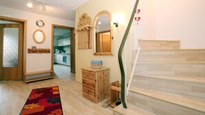Een kamer met een houten trap, een keuken op de achtergrond, een houten dressoir en een spiegel met houten lijst.