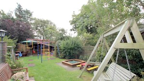 Een achtertuin met een houten schommel, een kleine speeltuin en een picknicktafel.