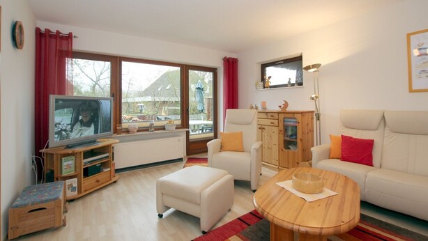 A living room with a television, sofa, armchair, wooden cabinet, and a window with a view. - Berliner Ring 24, Whg. 1 "Max" - vacation apartment in a 3-family house, approx. 95m², 3 (Wyk auf Föhr)