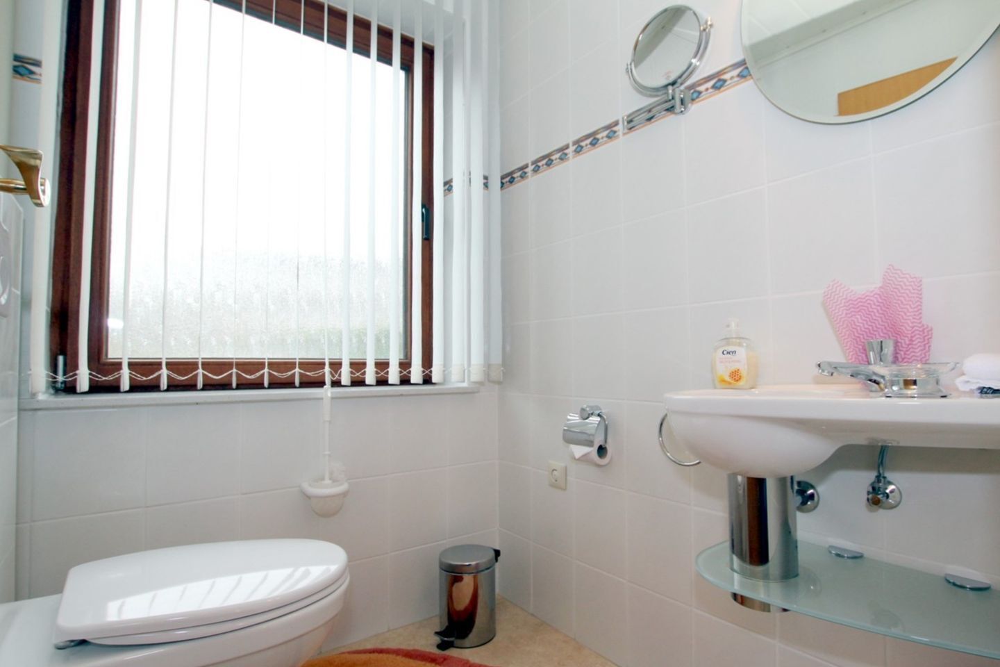 A bathroom with a toilet, a sink, a mirror, and a window with blinds.