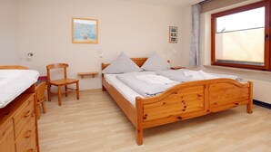 A bedroom with a wooden bed, a wooden dresser, a chair, a small table, and a window with blinds. - Berliner Ring 24, Whg. 1 "Max" - vacation apartment in a 3-family house, approx. 95m², 3 (Wyk auf Föhr)