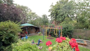 A backyard with a swing set, a playhouse, and a fenced area. - Berliner Ring 24, Whg. 1 "Max" - vacation apartment in a 3-family house, approx. 95m², 3 (Wyk auf Föhr)