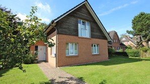 Une maison à deux étages avec une façade en briques, un toit en pente et un petit jardin à l’avant.