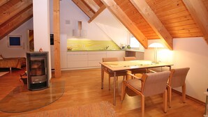 Une pièce mansardée chaleureuse, aménagée avec une table à manger, des chaises, un poêle à bois et un coin cuisine doté d’un plan de travail jaune.