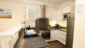 Een moderne keuken met een spoelbak, fornuis, oven en koelkast. Op de muur hangt een klok en boven de spoelbak een schilderij.