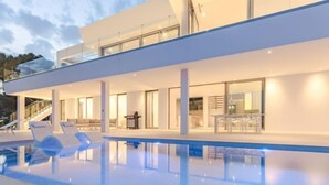 Ein modernes Haus mit Schwimmbad, Sitzgelegenheiten im Freien und einer Treppe, die zu einer zweiten Etage führt.