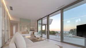Ein modernes Wohnzimmer mit einer großen Couch, einem Flachbildfernseher und einem Balkon mit Meerblick.