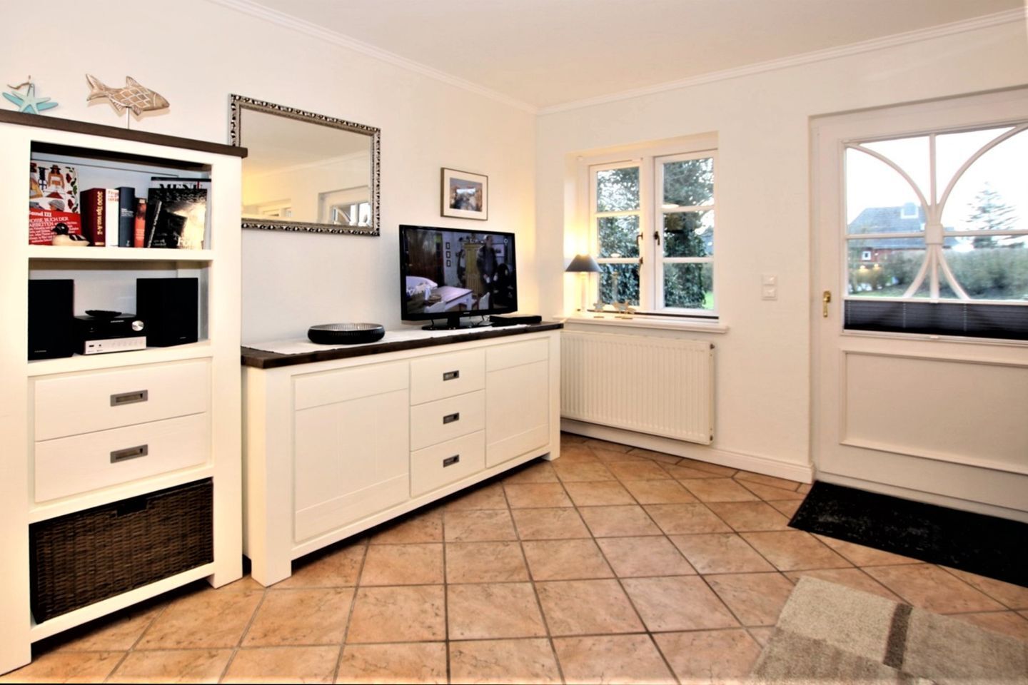 A compact kitchen with white cabinetry, a built-in TV, a small window, and a radiator.