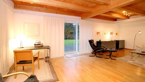 A modern living room with a wooden ceiling, a desk with a chair, a sofa, and a glass coffee table. - Am Grünstreifen 29, Haus Liguster Whg. no. 1 - vacation apartment in 2-family house, approx. (Wyk auf Föhr)