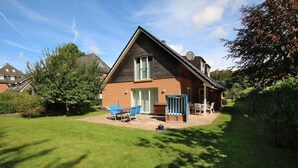 A two-story house with a sloped roof, a brick exterior, and a small backyard with a lawn, a patio with outdoor furniture, and a satellite dish. - Am Grünstreifen 29, Haus Liguster Whg. no. 1 - vacation apartment in 2-family house, approx. (Wyk auf Föhr)