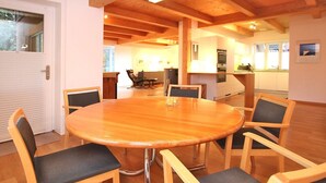 A round wooden table with six chairs in a room with wooden beams on the ceiling and a kitchen in the background. - Am Grünstreifen 29, Haus Liguster Whg. no. 1 - vacation apartment in 2-family house, approx. (Wyk auf Föhr)