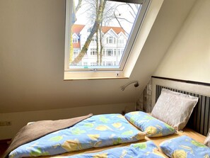 Ein Schlafzimmer mit Oberlicht, einem Bett mit floralem Bettzeug und Blick auf Gebäude.