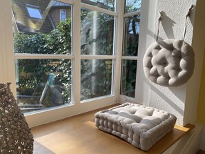Ein Zimmer mit großem Fenster, einer gepolsterten Bank und einem Hängekissen.