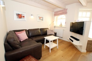 A living room with a brown leather sofa, a white coffee table, a flat-screen TV, and framed artwork on the wall. - Haus Kiebitz, Susanne-Fischer Weg 31 - 5 star vacation home with approx. 80 sqm (Wyk auf Föhr)