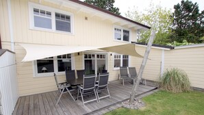 Ein Haus mit einer Terrasse, die einen Tisch, Stühle, einen großen Sonnenschirm und einen kleinen Baum zeigt.