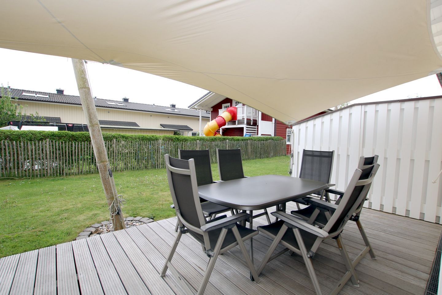 Une terrasse extérieure avec une table et des chaises, une terrasse en bois et, au fond, une clôture blanche.