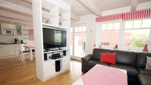 Ein modernes Wohnzimmer mit einer schwarzen Ledersofa, einem Fernseher auf einer weißen Unterhaltungseinheit und einem Essbereich mit einem weißen Tisch und Stühlen.