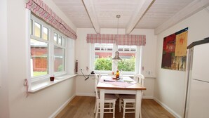Una cocina con una mesa de madera, sillas blancas, un refrigerador y una ventana con cortina a rayas.