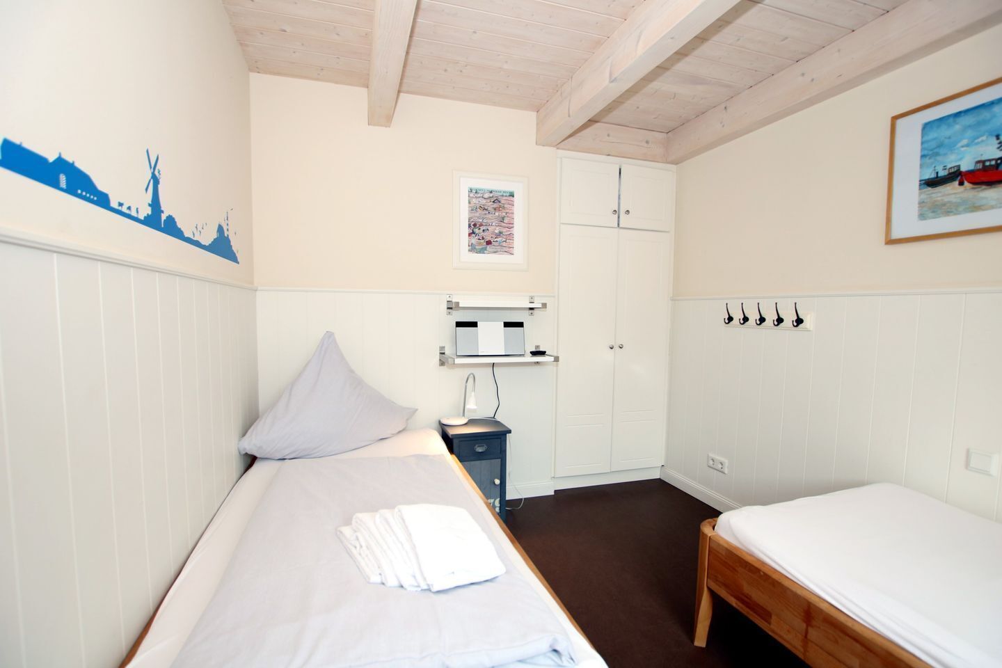 Ett sovrum med två enkelsängar, ett sängbord med en lampa, en garderob och en vägghylla med en tavla.