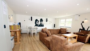 Ein geräumiges Wohnzimmer mit einem braunen Ecksofa, einem Holztisch und einem Essbereich mit weißen Stühlen.
