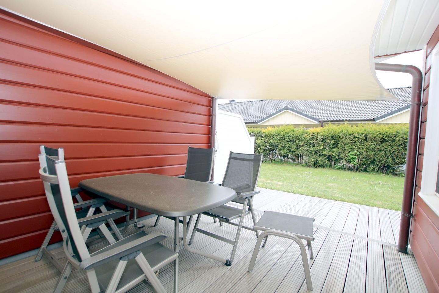 A covered outdoor patio with a table and chairs, a red wall, and a view of a house and garden.