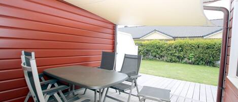 A covered outdoor patio with a table and chairs, a red wall, and a view of a house and garden.