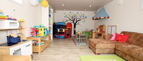 Un cuarto de juegos para niños con una tienda de campaña, juguetes, un sofá y una alfombra verde.