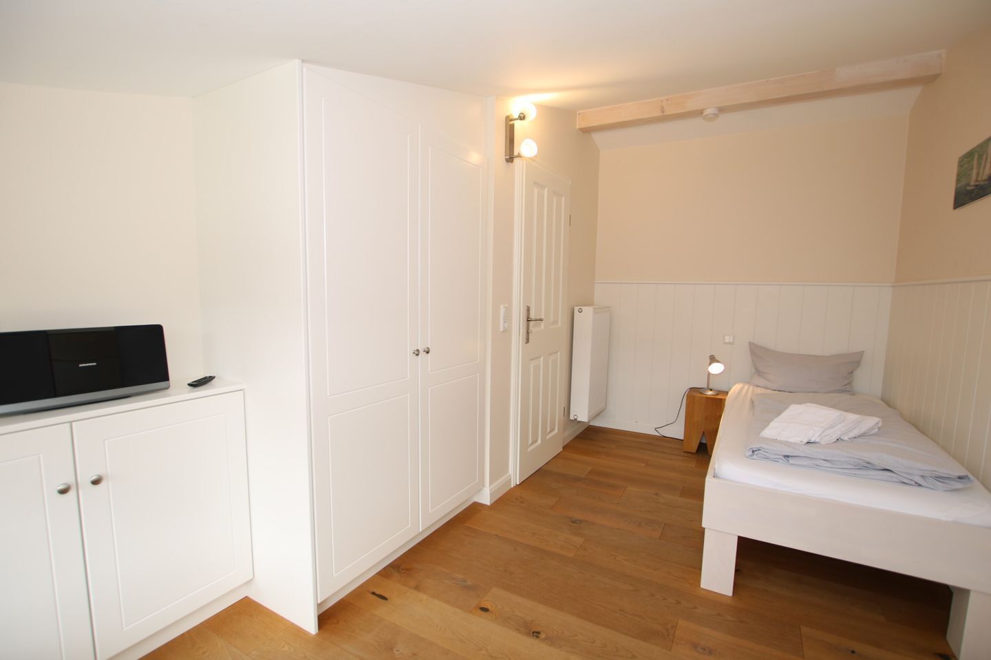A bedroom with a bed, a wardrobe, a radiator, and a bedside table with a lamp.