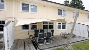 Een overdekt terras met een tafel en stoelen, een witte schutting en een houten terras.