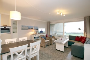 Uma sala de estar moderna com área de jantar, televisão e vista para o mar.