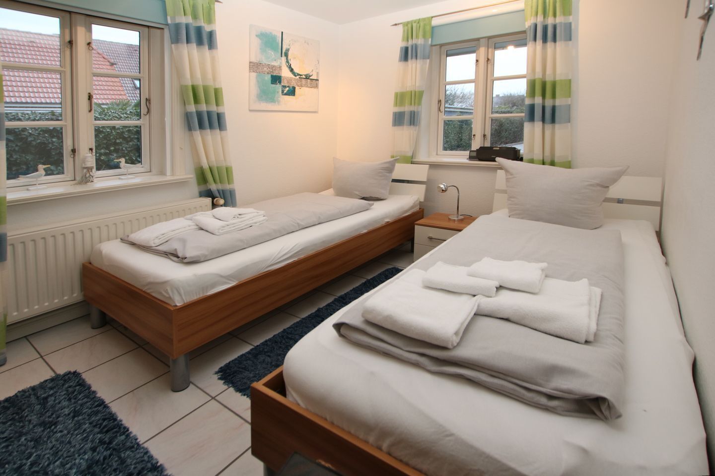 A bedroom with two single beds, a nightstand, a lamp, and a window with curtains.
