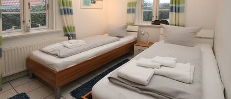 A bedroom with two single beds, a nightstand, a lamp, and a window with curtains.