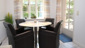 A dining area with a round table and four chairs, a window with curtains, and a potted plant on the windowsill. - Rungholtstraße 3c, Whg. 2 - Ferienwohnung mit 3- Zimmern auf ca. 65m² (Wyk auf Föhr)