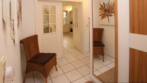 A hallway with a wicker chair, a door, and a mirror reflecting a chair. - Rungholtstraße 3c, Whg. 2 - Ferienwohnung mit 3- Zimmern auf ca. 65m² (Wyk auf Föhr)