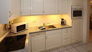 A kitchen with white cabinets, a microwave, a sink, and a built-in oven. - Rungholtstraße 3c, Whg. 2 - Ferienwohnung mit 3- Zimmern auf ca. 65m² (Wyk auf Föhr)