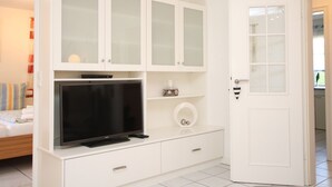 A room with a bed, a TV on a white cabinet, a toilet, and a door. - Rungholtstraße 3c, Whg. 2 - Ferienwohnung mit 3- Zimmern auf ca. 65m² (Wyk auf Föhr)