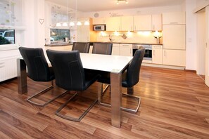Cozinha moderna com armários brancos, uma mesa de jantar com quatro cadeiras e piso de madeira.