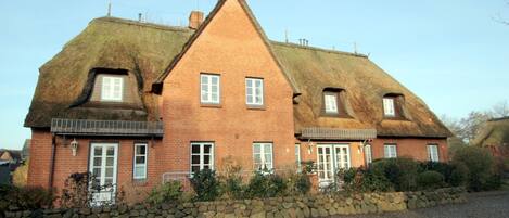 A two-story house with a thatched roof, a stone foundation, and a brick exterior.
