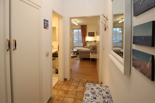 A hallway leading to a living area with a sofa, a table, and a lamp. There are doors on either side, and artwork on the walls. - Gmelinstraße 12, Whg. 7, Haus Meeresbrandung - Ferienwohnung mit 2-zimmern mit ca. 45m² und Balkon (Wyk auf Föhr)