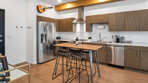 A modern kitchen with stainless steel appliances, wooden cabinets, and a bar stool area. - UPSCALE Cozy Nashville Condo★ POOL, PATIO, PARKING (Nashville)