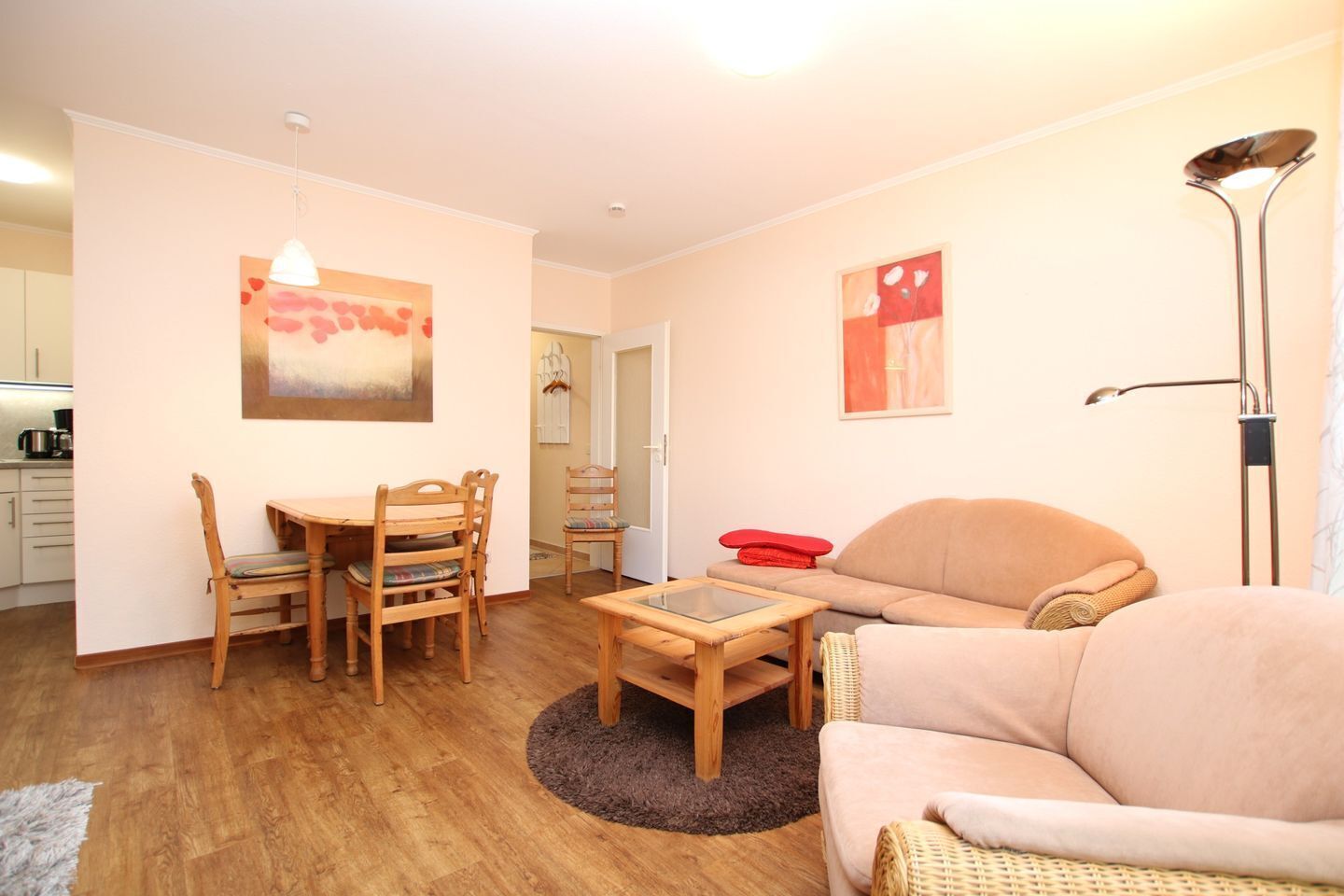A cozy living room with a sofa, a dining table with chairs, and a small coffee table. There is a kitchen area visible in the background.