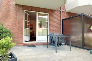 A patio area with a table and chairs, a sliding glass door, and a brick wall. - Gmelinstraße 12, Whg. 4, Haus Meeresbrandung - Holiday apartment with 2 rooms on (Wyk auf Föhr)