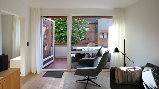A modern living room with a sofa, a chair, a small table, and a sliding glass door leading to a balcony. - Sandwall 60, Whg. 32, Huus in Lee - Holiday apartment on Sandwall with 3 rooms (Wyk auf Föhr)