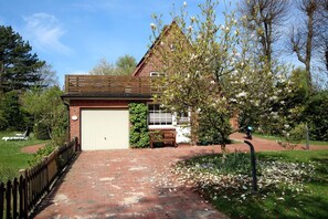 Una casa in mattoni con un garage, un recinto di legno e un giardino fiorito.