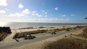 A beach with a road, benches, and a building. - Stockmannsweg 14, Whg.4 Haus am Meer - Ferienwohnung mit 3- Zimmern, ca. 80m² im 1. OG mit Blick auf (Wyk auf Föhr)