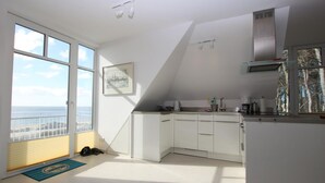 A modern kitchen with white cabinets, a built-in stove, and a view of the sea through large windows. - Stockmannsweg 14, Whg.4 Haus am Meer - Ferienwohnung mit 3- Zimmern, ca. 80m² im 1. OG mit Blick auf (Wyk auf Föhr)