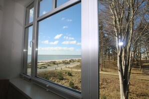 A window with a view of a beach, trees, and a clear sky. - Stockmannsweg 14, Whg.4 Haus am Meer - Ferienwohnung mit 3- Zimmern, ca. 80m² im 1. OG mit Blick auf (Wyk auf Föhr)
