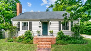 A single-story house with a green door, white siding, and a brick front porch.
