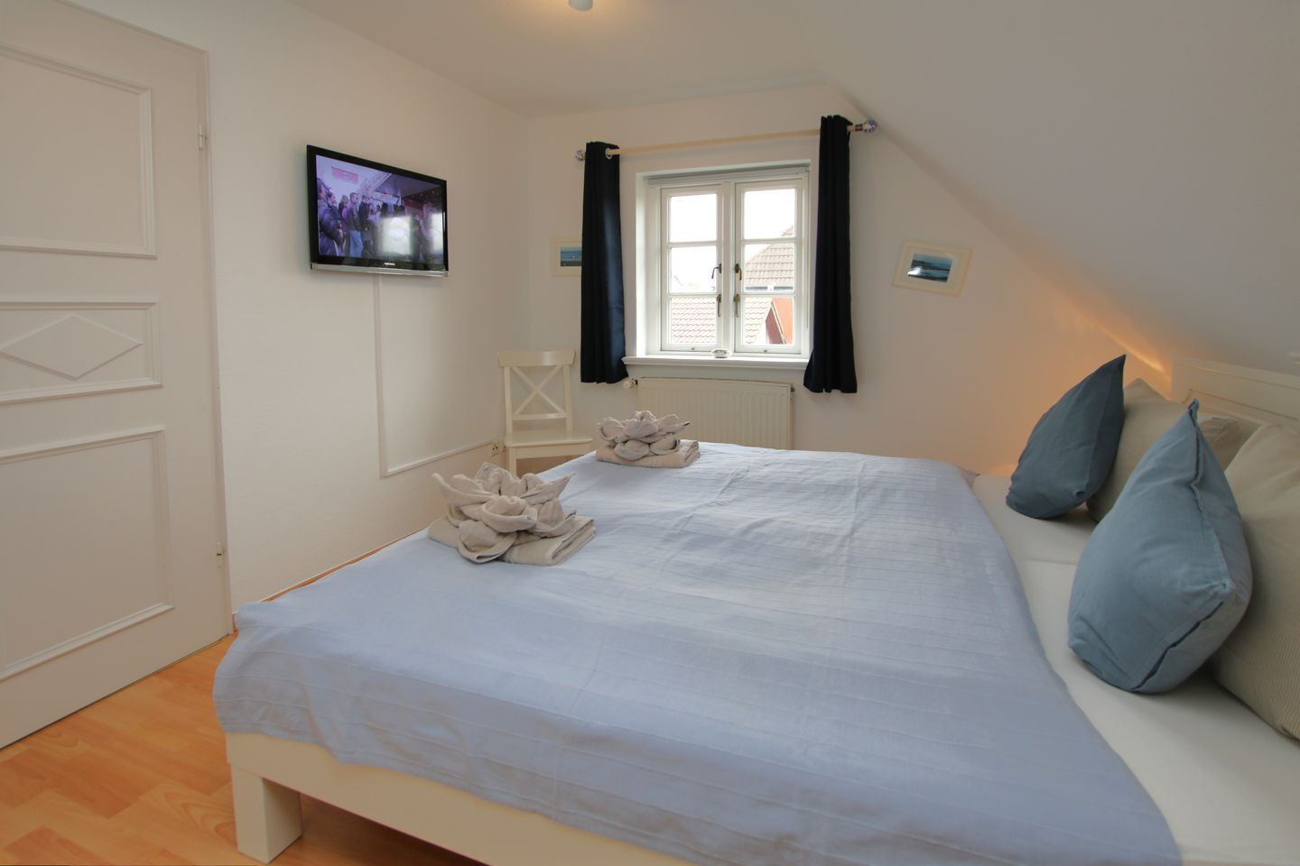 Une chambre à coucher avec un lit, des oreillers, une télévision, une fenêtre avec des rideaux et un radiateur.