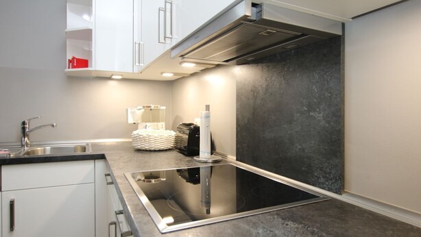A modern kitchen with a black induction cooktop, white cabinets, and a stainless steel sink. - Wiesenweg 4, Whg. 1, Wiesenkieker - Ferienwohnung mit 3- Zimmern auf ca. 76m² (Wyk auf Föhr)